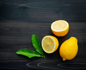 Fresh lemons and  lemons leaves on dark wooden background.