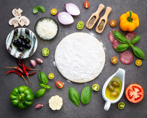 The ingredients for homemade pizza on dark stone background.