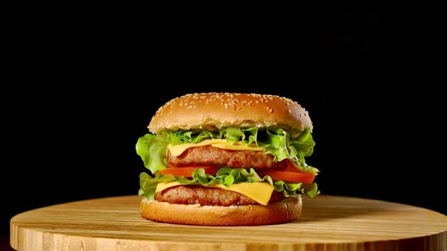 Fresh appetizing hamburger rotating on black background. Seamless loopable shot, 4k.