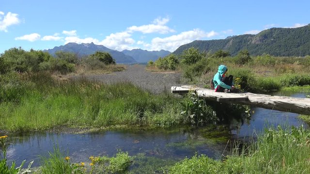 Girl is sitеing on a creek's wooden bridge near the Tromen Lake. Lanin NP, Patagonia, Neuquen, Argentina