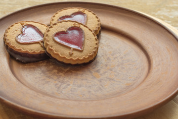 Sweet holiday cookies  with a red heart form filling on left side dark brown plate. Background for greeting card Valentine's day. Valentine day's present, sweet treat.
