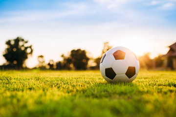 A ball on the green grass field for soccer football game under the sunset ray light.