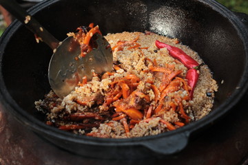 Pilaf prepare in big black cast iron with chefs hand. National cuisine concept.