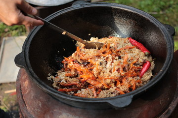 Pilaf prepare in big black cast iron with chefs hand. National cuisine concept.