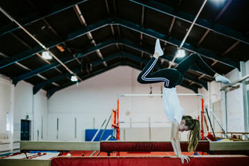 Female gymnast doing a handstand on a balance beam