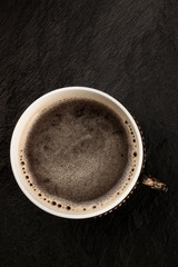 A photo of black coffee in a retro cup, shot from above on a dark background with copy space