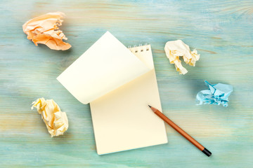In Search of Inspiration. An overhead photo of a spiral notepad with a blank sheet of paper and crumpled pages, shot from the top on a teal blue background with a graphite pencil and copy space