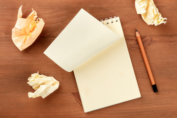Idea Crisis. An overhead photo of a spiral note pad with a blank sheet of paper and crumpled pages, shot from above on a dark wooden background with a graphite pencil and copy space © laplateresca