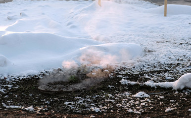 Steam is from sanitary sewer cover in snow, accident. Side view.