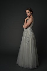 Fototapeta premium full length portrait of brunette girl wearing long silver ball gown. standing pose on grey studio background.