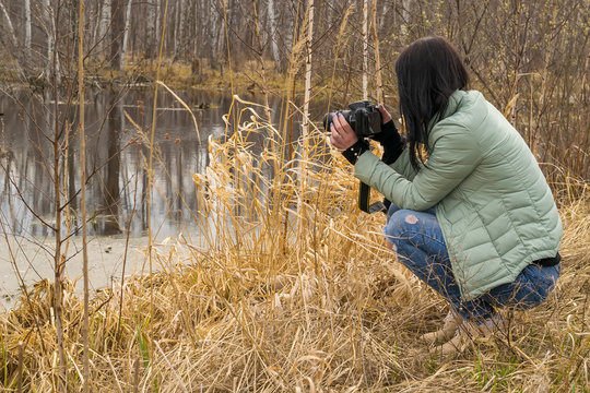 A girl in a warm jacket in the spring photographs objects near the pond
