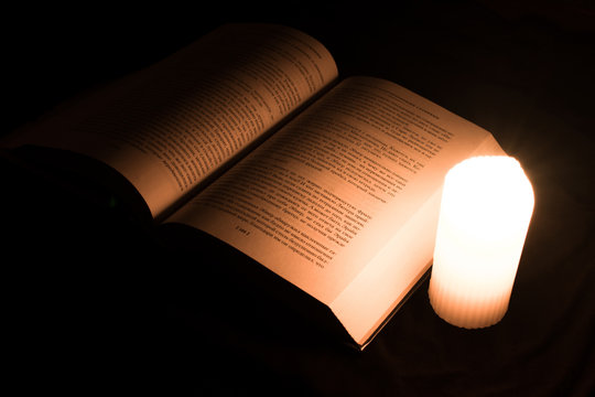 Old Foreign Book And Burning Candle. Reading By Candlelight. Warm And Romantic Atmosphere