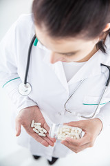 Female doctor on white background  spills pills from jar to the hand. Vertical view