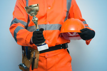 Best builder contractor award concept. Golden cup trophy in the worker hands isolated on blue...