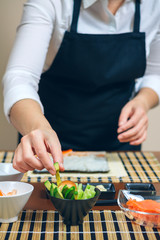 Unrecognizable female chef taking sliced avocado from among the ingredients prepared to make sushi