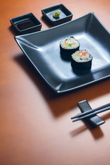 Sushi maki rolls presented on a plate with sauces and chopsticks