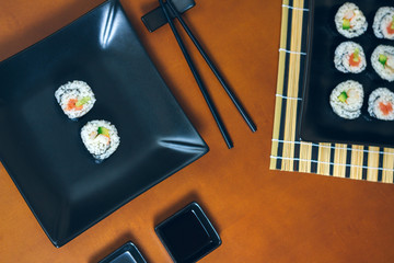 Sushi maki rolls presented on a plate and tray with sauces and chopsticks