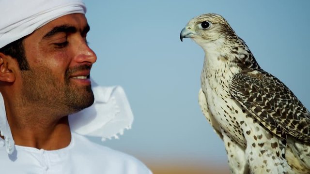 Trained falcon tethered to male owner wearing traditional Arabic dress 