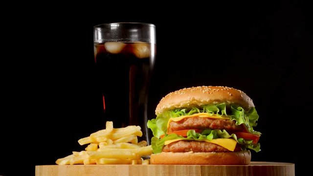 burger with french fries and a glass with ice cola on a black rustic background
