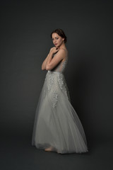 full length portrait of brunette  girl wearing long silver ball gown. standing pose on grey studio background.