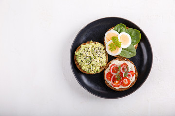Different kinds of whole grain bread sandwiches on black plate.