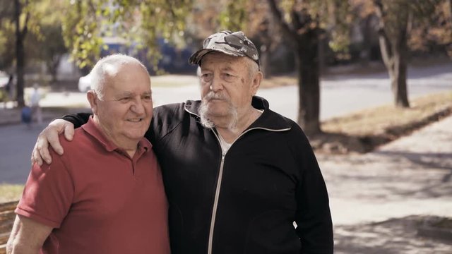 Portrait of aged lonely, but happy men friendly embracing at camera on street