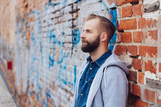 Thoughtful casual man leaning on grunge brick wall