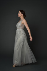 Fototapeta premium full length portrait of brunette girl wearing long silver ball gown. standing pose on grey studio background.