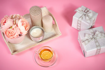 peonies, candles on a wooden tray, tea and gifts on a light pink background