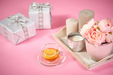 peonies, candles on a wooden tray, tea and gifts on a light pink background