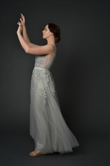 Fototapeta premium full length portrait of brunette girl wearing long silver ball gown. standing pose on grey studio background.