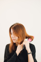Close up of hands drying woman hair with equipment. The asian woman brown hair in a black shirt is holding Hair straighteners.