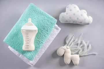 Feeding bottle of milk for baby with towels and toys on grey background