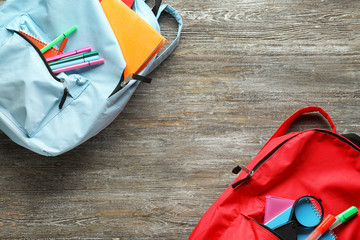 Naklejka premium Color rucksacks with school stationery on wooden background