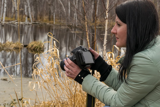A girl in a warm jacket in the spring photographs objects near the pond