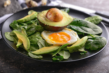 Tasty fried egg with avocado and spinach on plate