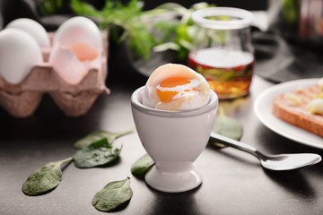 Holder with tasty boiled egg on dark table
