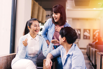 South East Asian senior mother holding a cup of coffee with young man and woman talking with laugh and happiness indoors