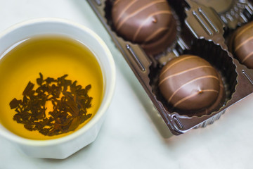 A mug of tea with chocolate dessert on a light table.