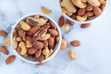 roasted mixed nuts in white ceramic bowl on barble table background.