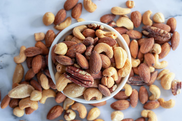 roasted mixed nuts in white ceramic bowl on barble table background.