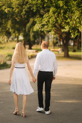Young beautiful couple husband in a white shirt and a woman in a dress walking around the park in summer time