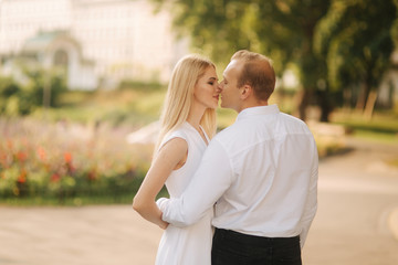 Young beautiful couple husband in a white shirt and a woman in a dress walking around the park in summer time