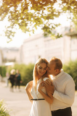 Fototapeta premium Young beautiful couple husband in a white shirt and a woman in a dress walking around the park in summer time