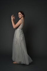 Naklejka premium full length portrait of brunette girl wearing long silver ball gown. standing pose on grey studio background.