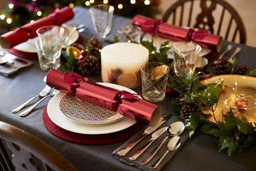 Close up of Christmas table setting with Christmas crackers arranged on plates and red and green...