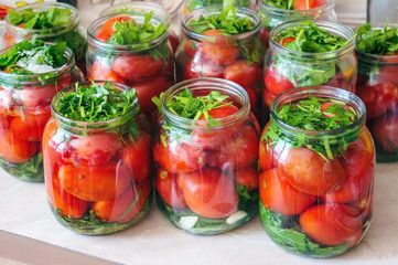 Fermenting vegetables with lots of greens in glass jars. Processing the harvest of tomatoes from home garden