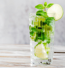 Mojito cocktail on white wood background in a faceted transparent glass close up