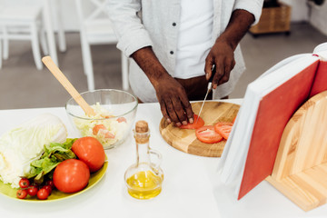 african american man slicing tomatoes on wooden chopping board