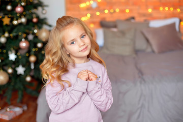 Beautiful girl with blond curls in anticipation of gifts in the background Christmas lights and bed . New Year and Christmas concept.